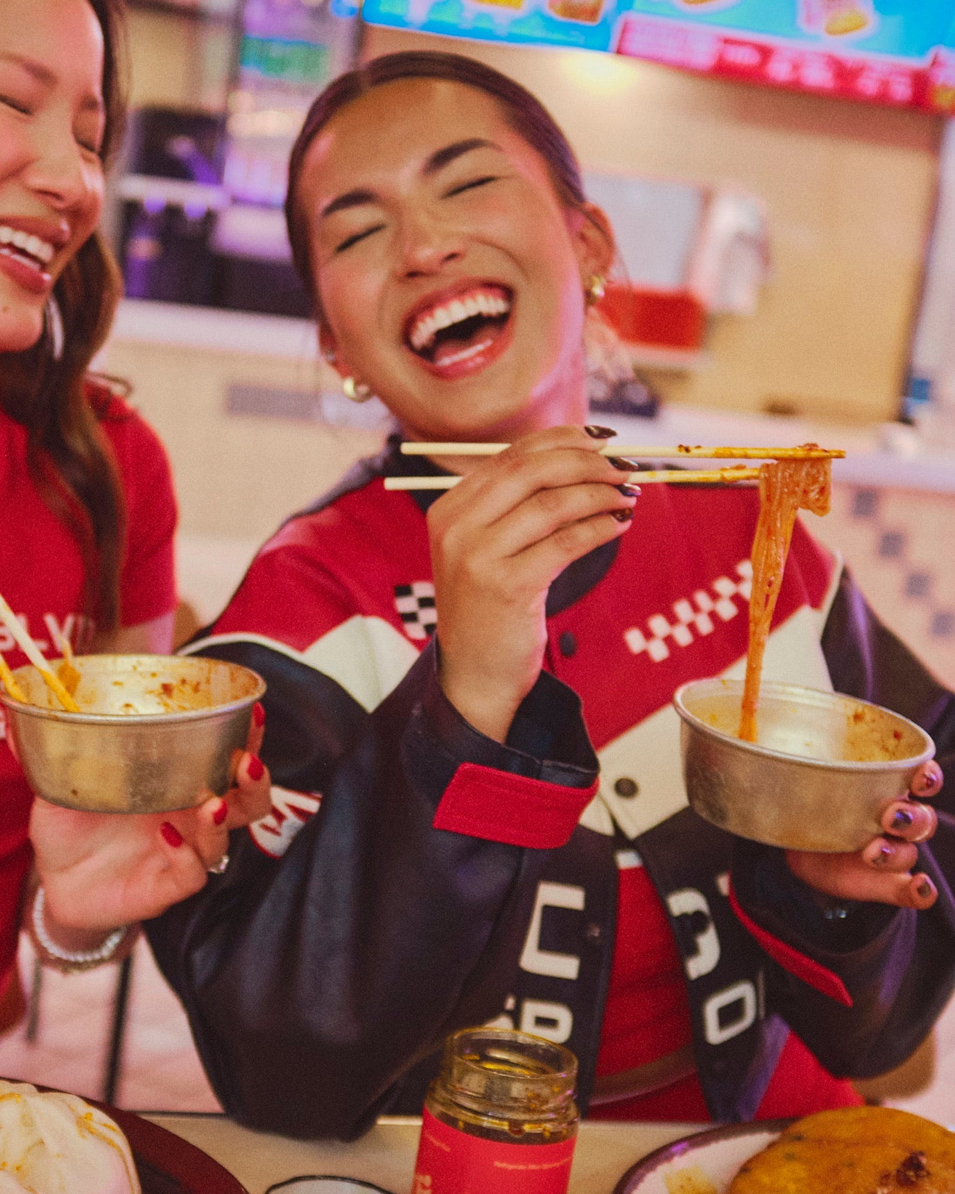 Two friends smiling while dining at Korean food court, eating noodles with Hot Girl Crunch Chili Oil - Hotgirlsauce chili oil - chili sauce - hot sauce