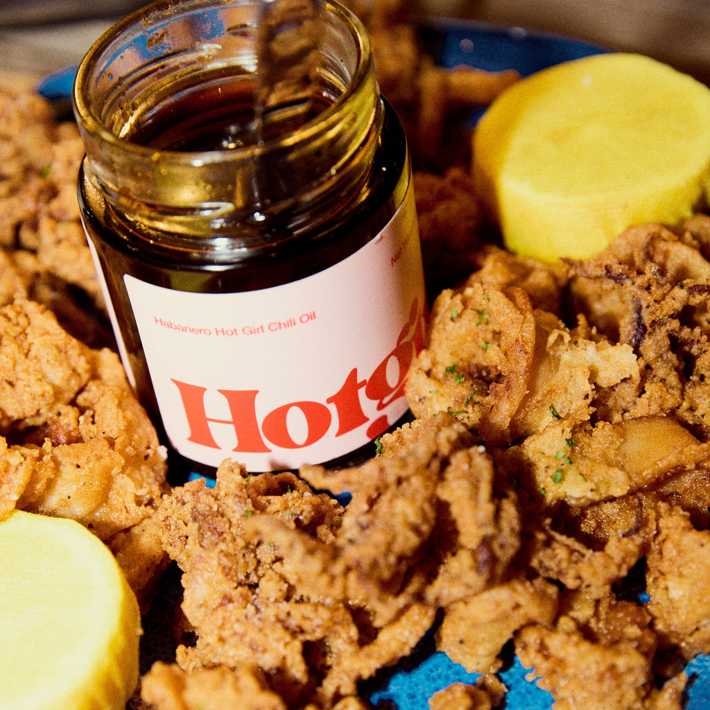 Jar of Habanero Hot Girl Chili Oil next to lemon on a plate of fried calamari  -  Hotgirlsauce chili oil - chili sauce - hot sauce