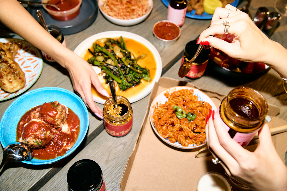 Two girls drizzling Hotgirlsauce chili oils over pasta, veggies, and Italian foods -  Hotgirlsauce chili oil - chili sauce - hot sauce