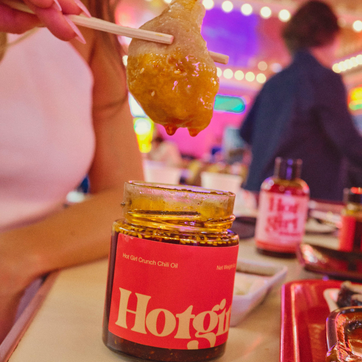 Woman dunkin a dumpling into a jar of Hot Girl Crunch Chili Oil hot sauce in a food court -  Hotgirlsauce chili oil - chili sauce - hot sauce