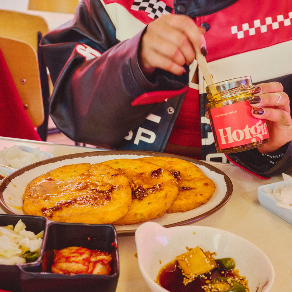 Woman drizzling Hot Girl Crunch Chili OIl over plate of Korean pancakes in food court -  Hotgirlsauce chili oil - chili sauce - hot sauce