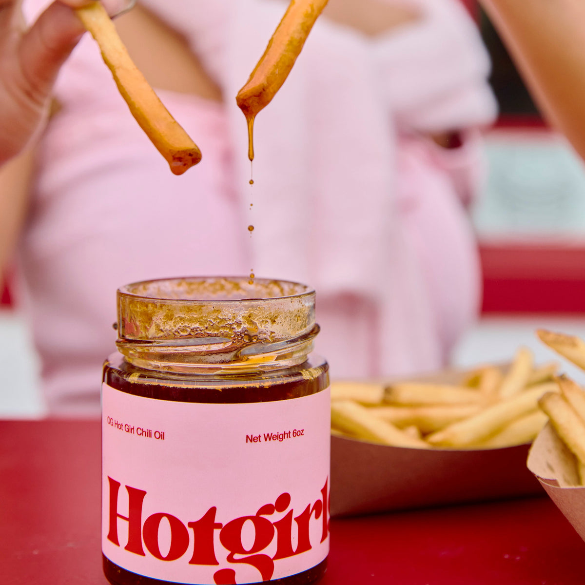 Person dipping a french fry into a jar of OG Hot Girl Chili OIl hot sauce with another fry held above it -  Hotgirlsauce chili oil - chili sauce - hot sauce