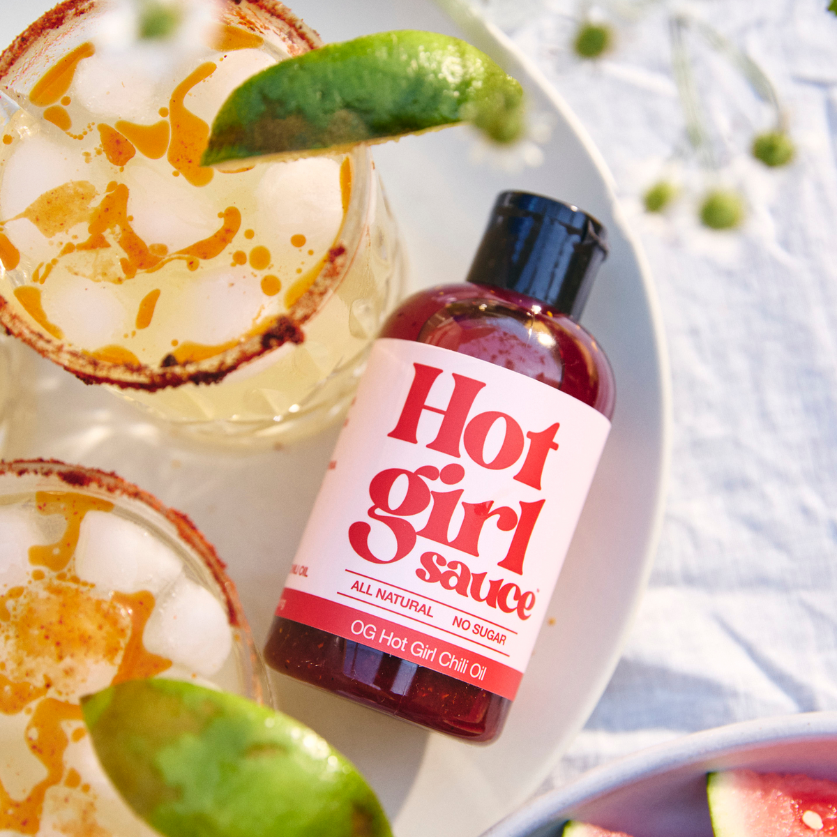 Bottle of OG Hot Girl Squeezable Chili Oil next to two margaritas drizzled in chili oil - Hotgirlsauce chili oil - chili sauce - hot sauce