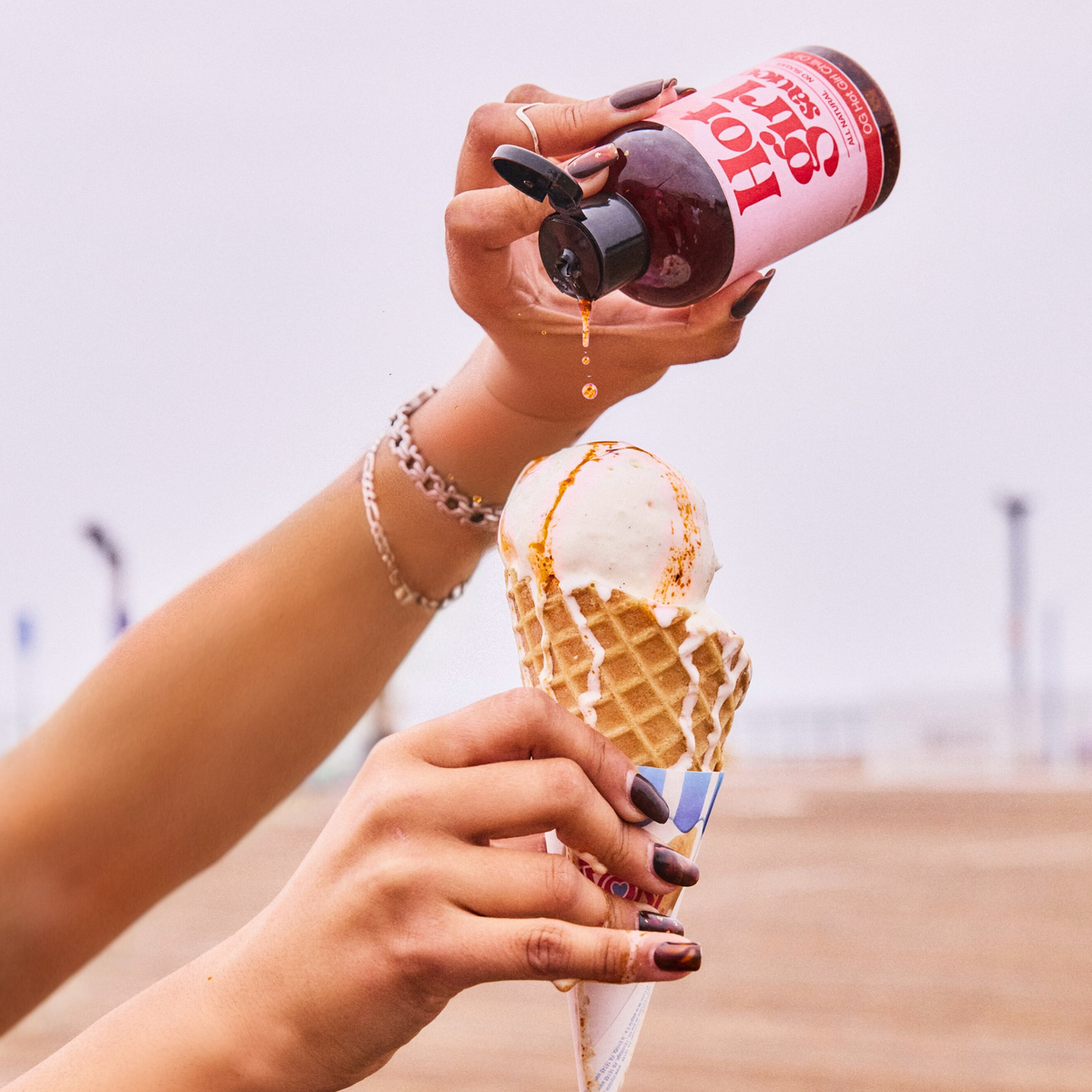 Woman squeezing OG Hot Girl Chili Oil over ice cream cone while at the pier by the beach -  Hotgirlsauce chili oil - chili sauce - hot sauce