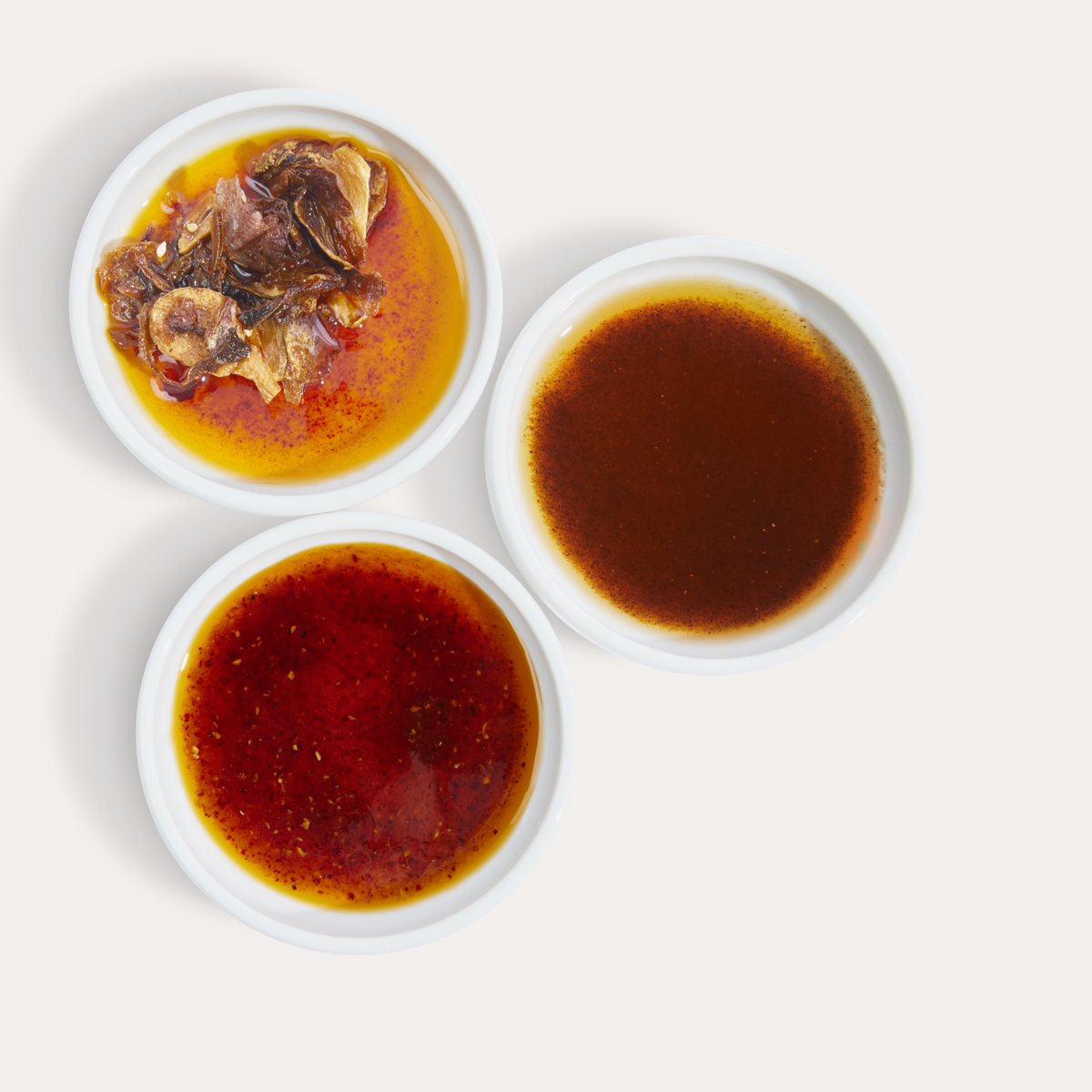 Hot Girl Trio of Chili Oil poured into saucers - one with OG Hot Girl Chili Oil, one with Habanero Hot Girl Chili Oil, and one with Hot Girl Crunch Chili Oil - Hotgirlsauce chili oil - chili sauce - hot sauce